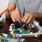Man working on an electronic circuit board with tools on a table