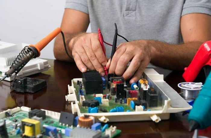 Man working on an electronic circuit board with tools on a table
