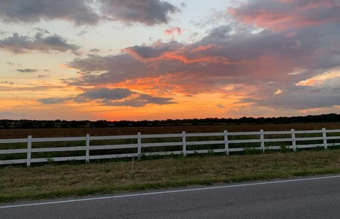 Sunset over a Texas pasture with a white fence lining the road